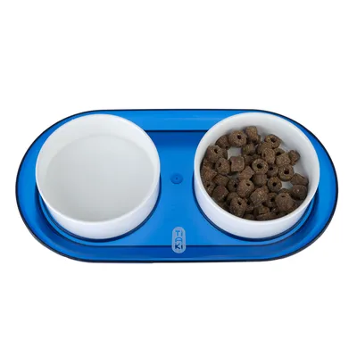 Doppelnapf-Set mit blauem Untersetzer, zwei weissen Schalen: eine mit Wasser, die andere mit braunen Trockenfutterringen. Marke Tiaki sichtbar auf dem Untersetzer.