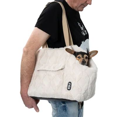 Sac de transport beige en tissu Tiaki porté à l’épaule, avec un petit chien à l’intérieur. Marque Tiaki visible sur le sac.