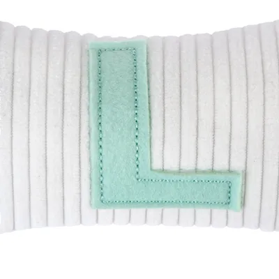 Bílý polštář s prošívanou látkou a zeleným plstěným písmenem L na povrchu.