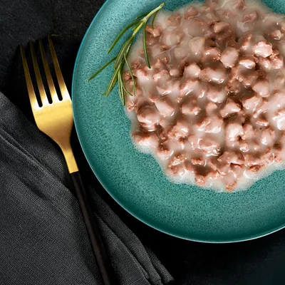 Close-up of served wet food on a green plate with a sprig of rosemary, next to a gold fork and black napkin.