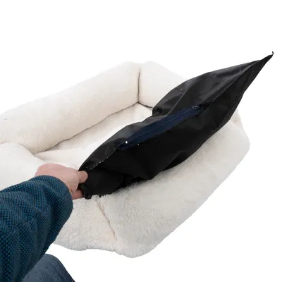 Hand showing removable inner cushion with zip from a white pet bed.