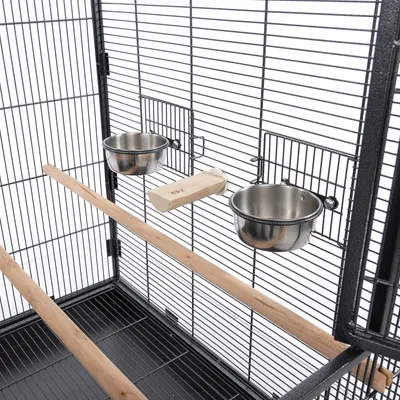 Indretning til fuglebur med to foder- og vandskåle i rustfrit stål, siddepinde i træ og en træplatform. Metalskabsstruktur synlig.