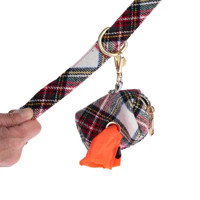 Pochette à motif écossais accrochée à une laisse, contenant des sacs orange pour déjections canines. Mousqueton et anneau dorés visibles.