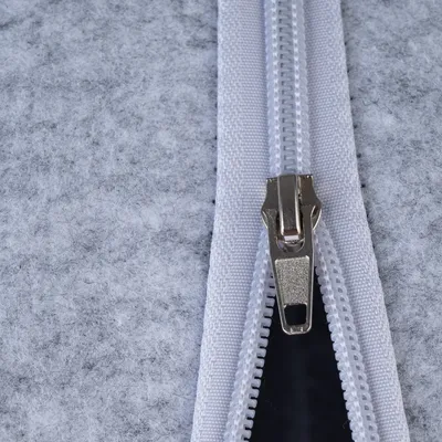 Close-up de um fecho éclair branco com cursor prateado em feltro cinzento.