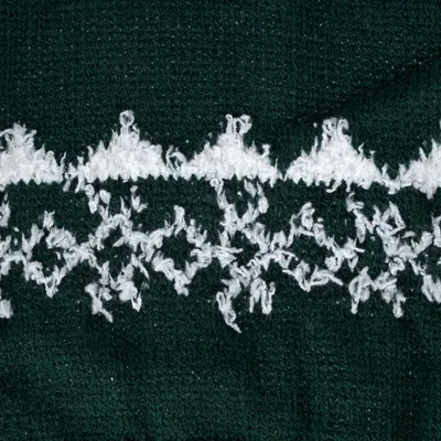 Nahaufnahme eines gestrickten Materials in dunkelgrün mit weissem, flauschigem Muster. Keine weiteren Produktinformationen sichtbar.