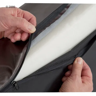 Detail van hondenbed met geopende rits, zicht op witte schuimvulling en afneembare hoes van kunstleer en stof.