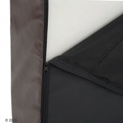 Detail van een hondenbed met afneembare hoes, zichtbaar rits en schuimvulling. Hoes van kunstleer en stof in zwart en bruin.