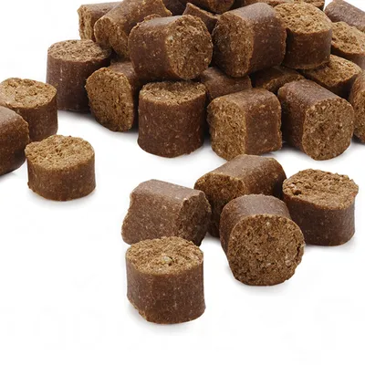 Hnědé válečkové granule nebo pamlsky pro domácí mazlíčky, detailní pohled na strukturu a tvar jednotlivých kusů bez viditelného obalu či značky.