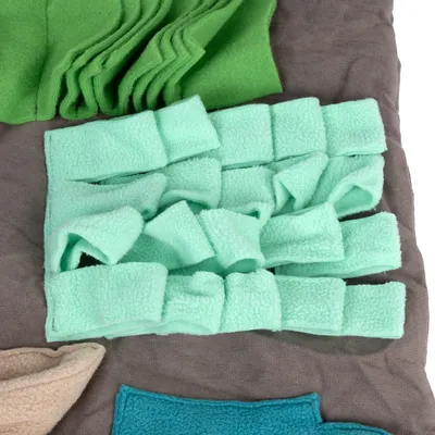 Product image of green and mint-coloured fleece material, cut into strips and shapes, on a grey background.