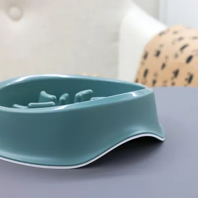 Turquoise feeding bowl with raised inner structures to slow eating, made of plastic on a grey surface.