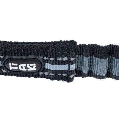 Zbliżenie na czarno-szarą obrożę z odblaskowymi paskami i logo z napisem 'TIEKI'.