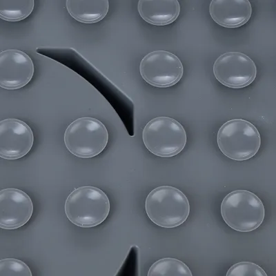Surface grise avec ventouses rondes en plastique, vue rapprochée d’un tapis antidérapant pour animaux. Détail des reliefs et d’une découpe en forme de courbe visible.