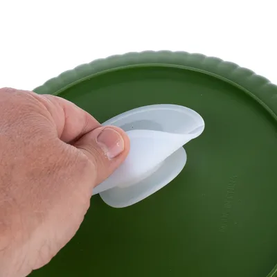 Hand lifts white silicone lid from green container. Text on container: Made in China.