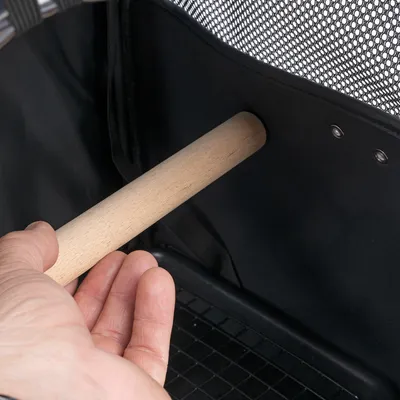 Hand toont het monteren van een houten staaf in een zwarte transportbox met netstof en metalen klinknagels.