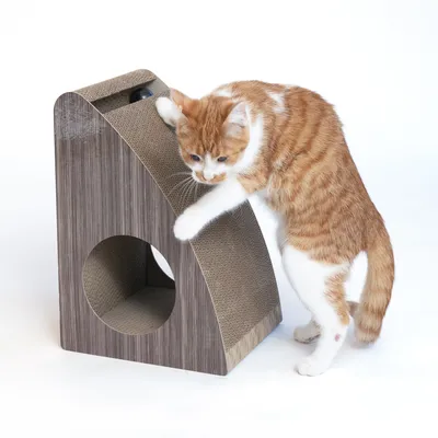 Brown scratching furniture made of cardboard with a round entrance and slanted scratching surface, demonstrated by a red and white cat.