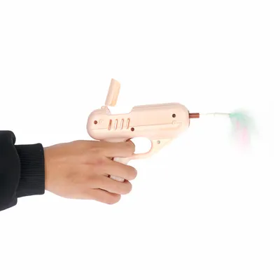 Hand hält eine beige Spielzeugpistole mit Federaufsatz in Pastellfarben, geeignet für interaktives Spielen.