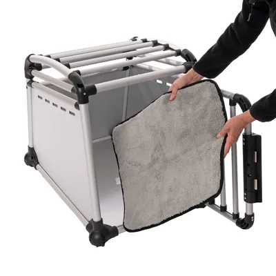 Transportbox aus Metall mit abnehmbarem, grauem Polster. Person zeigt das Herausnehmen des Polsters.