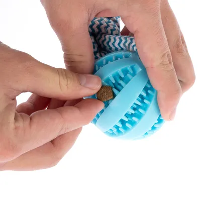Manos colocando una golosina en una pelota de juego azul con protuberancias. Demostración de llenado del juguete.