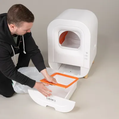 Demonstration of cleaning a white kooa cat litter box with pull-out drawer and orange frame.