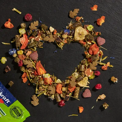 Vitakraft small animal food with dried fruits, vegetables and herbs arranged in heart shapes. Packaging corner with visible Vitakraft logo.