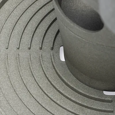 Primer plano de una superficie gris y texturizada con ranuras circulares y un elemento cilíndrico.