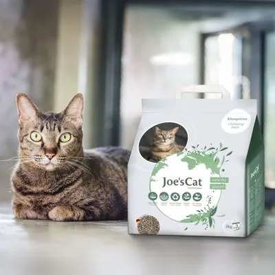 Zak kattenbakvulling met merknaam Joe'sCat, zichtbaar: klonterende variant, 3 kg, afbeelding van kat op de verpakking, diverse pictogrammen en groene wereldkaartdecoratie.