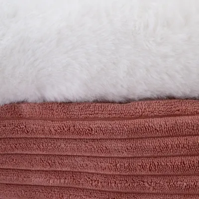 Gros plan sur un lit ou coussin pour animal avec dessus en tissu blanc duveteux et côtés en tissu côtelé rose. Deux textures visibles : peluche et tissu bouclé.