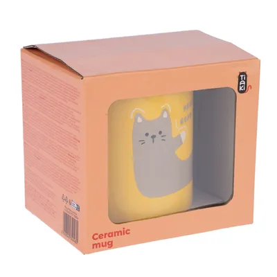 Tasse en céramique Tiaki avec motif de chat gris sur fond jaune, visible dans une boîte rose avec fenêtre transparente. Texte visible : Ceramic mug.