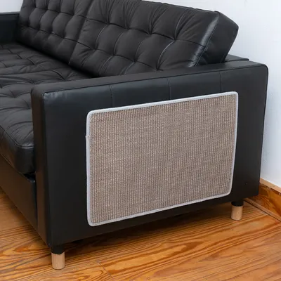 Alfombrilla protectora de sisal, fijada al lateral de un sofá de cuero negro. La alfombrilla protege los muebles de arañazos.