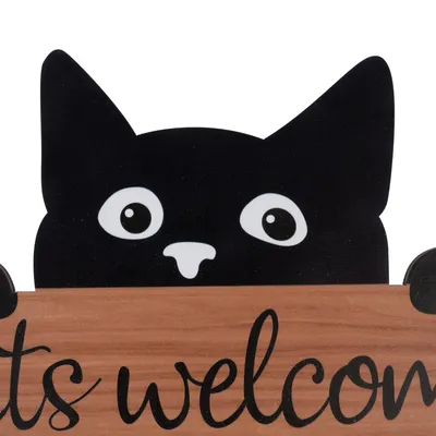 Fekete macska nagy szemekkel egy fa táblánál, amelyen az áll: 'Cats welcome'.