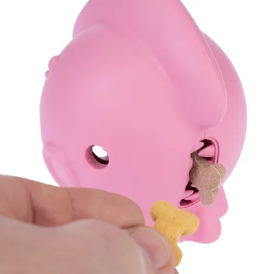 Main insérant une friandise en forme d’os dans un jouet distributeur rose pour animaux, ouverture visible avec une autre friandise à l’intérieur. Jouet en plastique.