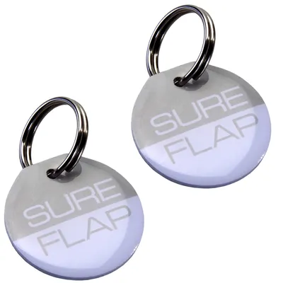 Due medagliette rotonde con anello metallico, testo visibile: SURE FLAP