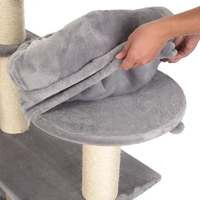Arbre à chat en tissu gris avec coussin amovible, main soulevant le coussin sur une plateforme ronde, poteaux recouverts de corde visible.