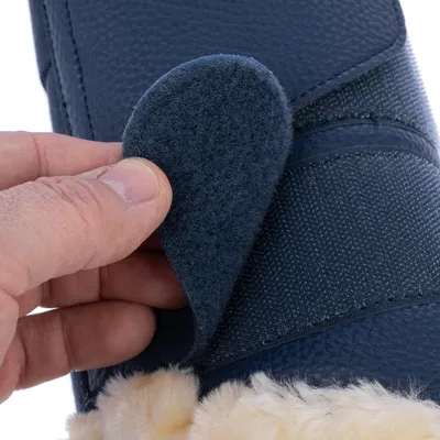 Gros plan sur une main ouvrant une fermeture à scratch sur une botte bleue en tissu avec doublure intérieure en fourrure synthétique beige visible.