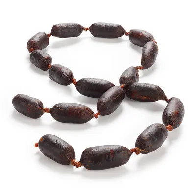 Saucisses sèches pour animaux, reliées en une longue chaîne, couleur foncée, sans marque visible, présentées sur fond blanc.
