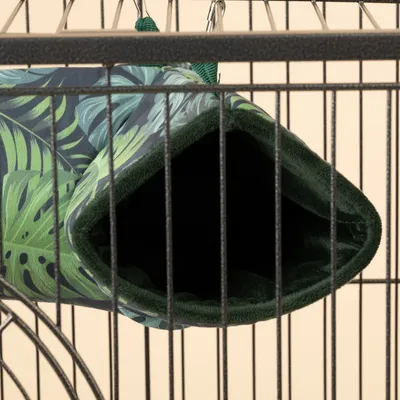 Hamaca con estampado de hojas tropicales, forro verde, sujeta a jaula metálica con ganchos.