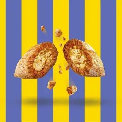 Przekrojony na pół chrupiący przysmak z jasnym nadzieniem, widoczne kawałki wypadające ze środka. Tło w żółto-niebieskie pasy.