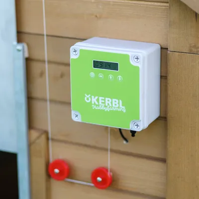 Kerbl Hobbyfarming control automat pentru ușă cu afișaj digital și panou frontal verde, montat pe suprafață de lemn.