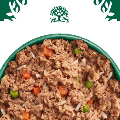 Close-up of wet food with meat pieces, carrots, peas and rice in a green bowl. Logo with tree, dog and cat visible at the top.