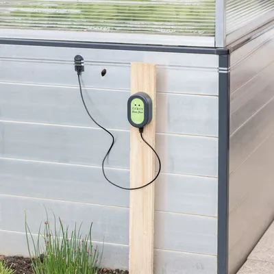 Elektronisches Schneckenabwehrgerät Snail Stop, montiert an einem Holzpfosten neben einem Gewächshaus. Kabel und Sensor sichtbar.