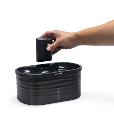 Distributeur automatique noir beeztees avec deux compartiments, une main place un module amovible sur le dessus. Matériau plastique visible.