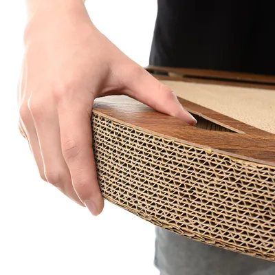 Hand holding a product made of corrugated cardboard with a wood look. Close-up of material texture and handle opening.