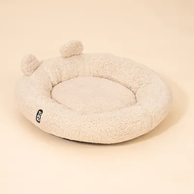 Rundes, beiges Liegekissen aus Plüsch mit erhöhtem Rand und zwei kleinen Ohren. Sichtbares Etikett mit der Aufschrift 'FGY'. Rundes, beiges Liegekissen aus Plüsch mit erhöhtem Rand und zwei kleinen Ohren. Sichtbares Etikett mit der Aufschrift 'FGY'.