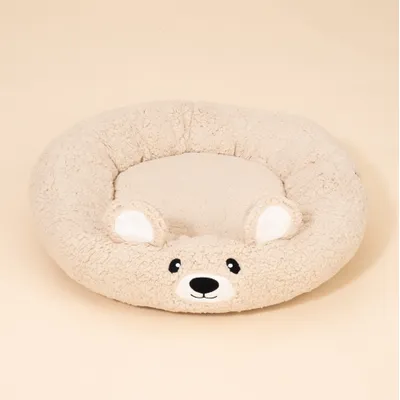 Rundes, beiges Kuschelbett mit Bärenkopf-Design und aufgesticktem Gesicht sowie zwei abstehenden Ohren. Flauschige Oberfläche. Rundes, beiges Kuschelbett mit Bärenkopf-Design und aufgesticktem Gesicht sowie zwei abstehenden Ohren. Flauschige Oberfläche.