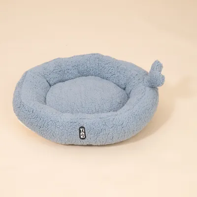 Rundes, hellblaues Bett aus weichem Stoff mit Tiaki-Label und Knoten am Rand.