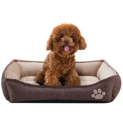 Bruin hondenbed met beige binnenkant, zichtbaar pootafdrukmotief op de voorkant. Kleine bruine hond zit in het bed.