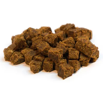 Peças de ração seca castanhas em forma de cubo dispostas soltas sobre fundo branco.
