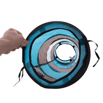 Hand hält zusammenklappbaren Tunnel aus blauem und braunem Stoff mit schwarzem Rand, geeignet für Spiel oder Transport.