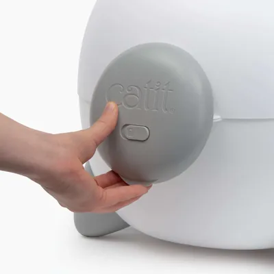 Hånd aktiverer grå kontakt med catit-logo på en hvid enhed.