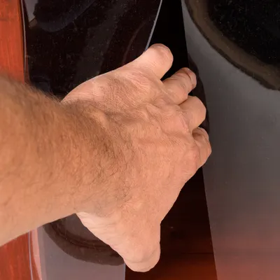 Mano de una persona levantando una tapa o panel negro brillante, posiblemente de plástico o vidrio, sobre una superficie marrón. No se observan marcas ni texto visible.